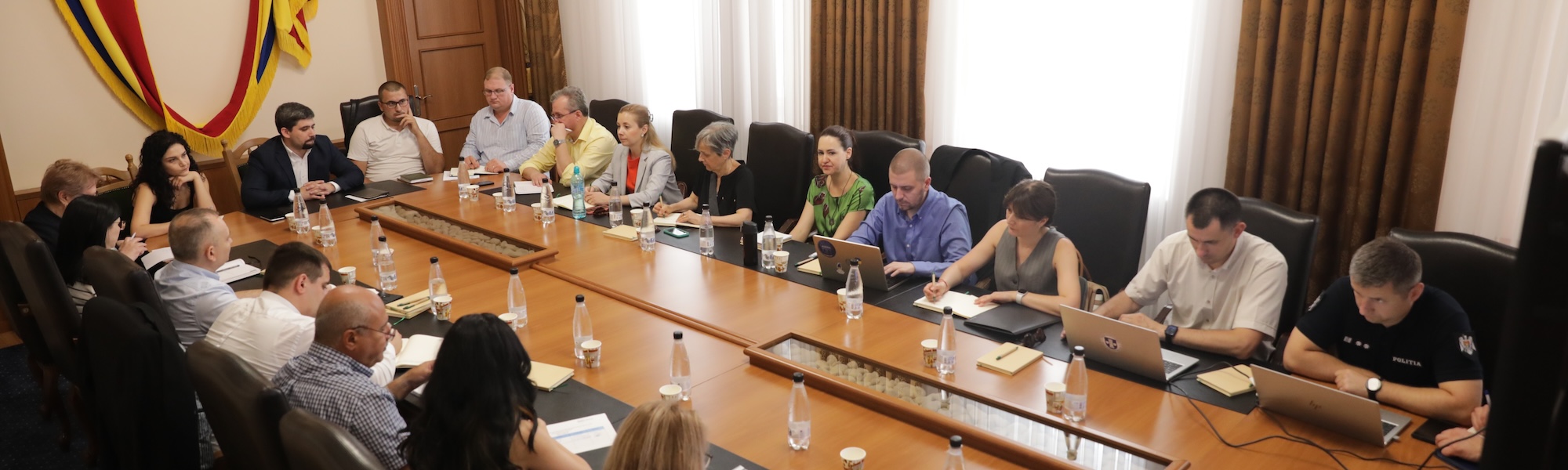 Meeting of stakeholders in boardroom with Moldovan flag on wall